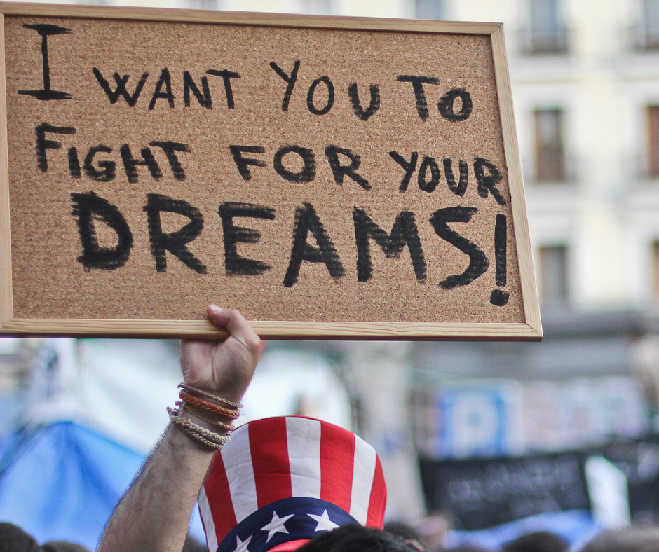 Person wearing American flag hat holding sign that reads: I want you to fight for your dreams!